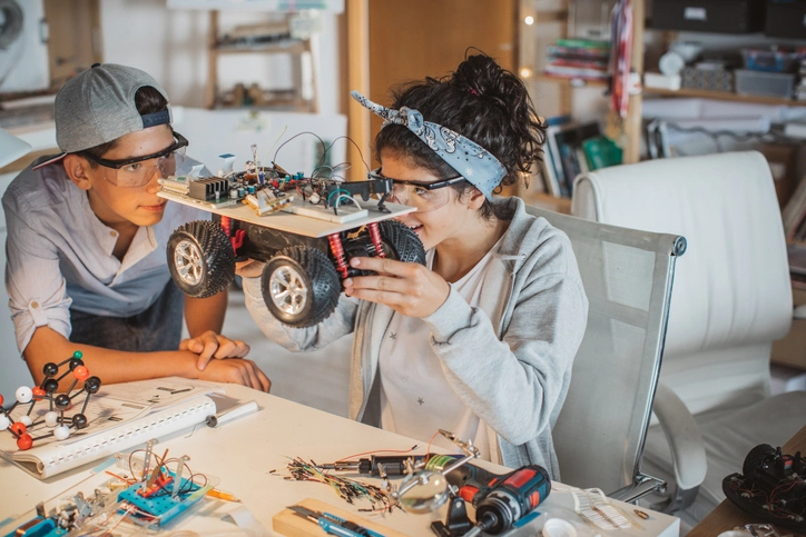 Two teenagers building a electric car with electronic equipment wearing protective eyegear