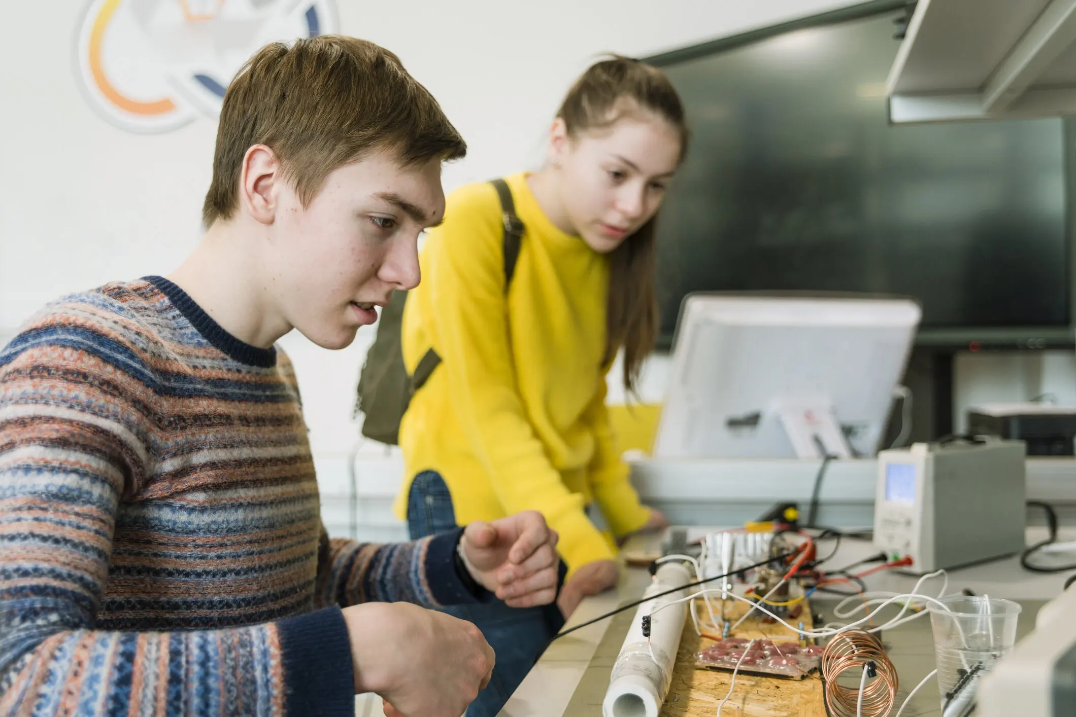 Teenage boy working on some electronic device while girl is watching