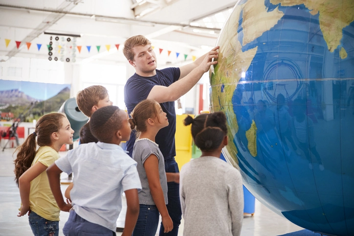 Teacher pointing at a giant globus and his students watch eagerly