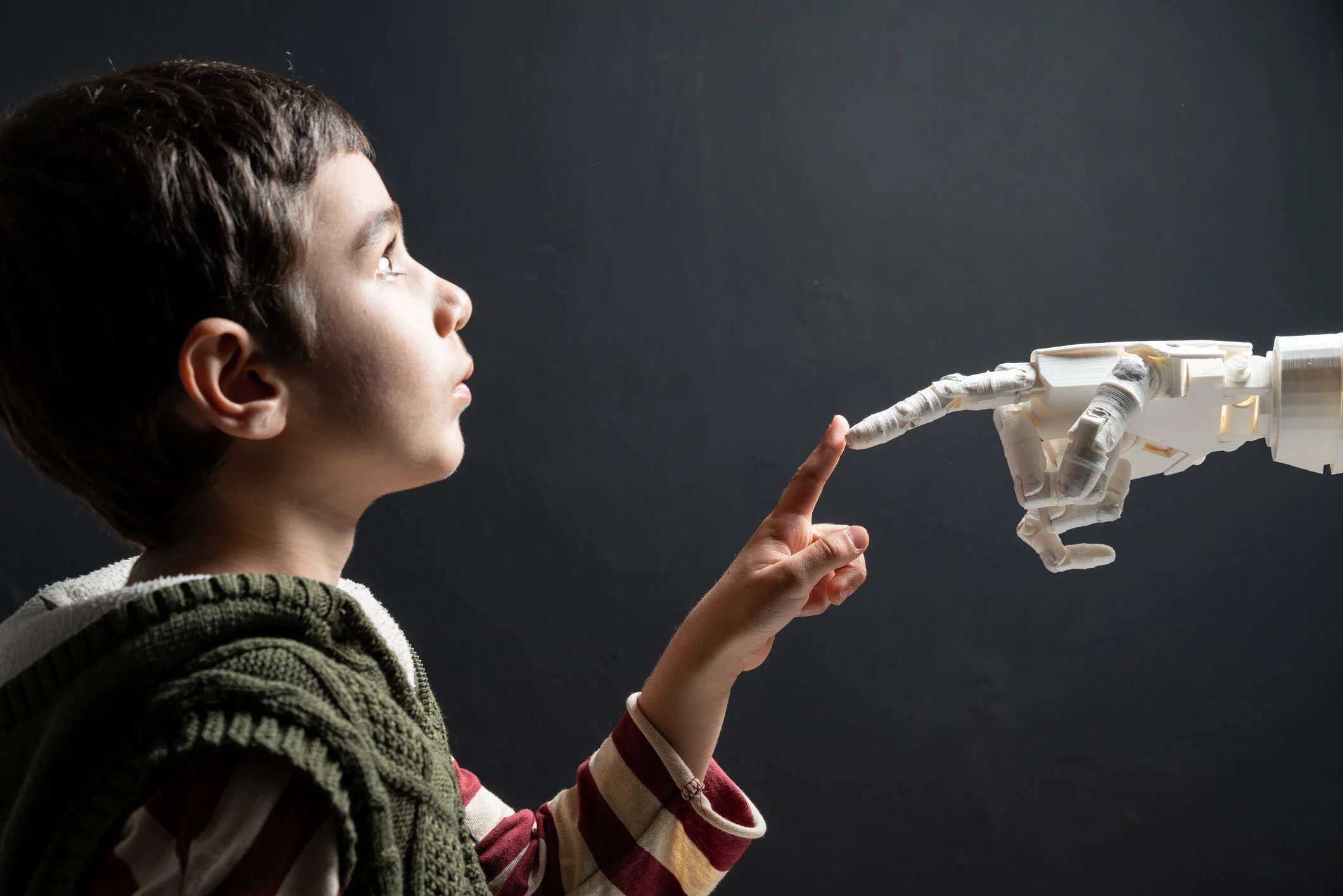 Boy looking up and touches a white robot hand