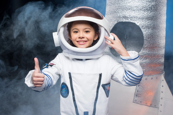 Little girl in a astronaut suit smiling and giving a thumbs up